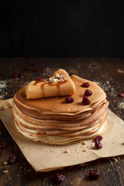 yığın krep katlanmış, gözleme, çilek, kurabiye, pudra şekeri ve koyu ahşap bir masa üzerine parşömen üzerine karamel şurup serpilir