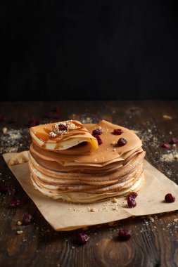 yığın krep katlanmış, gözleme, çilek, kurabiye, pudra şekeri ve koyu ahşap bir masa üzerine parşömen üzerine karamel şurup serpilir