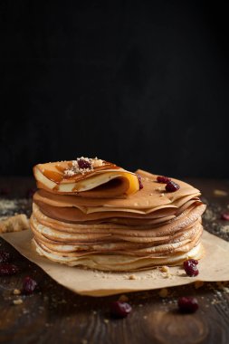 yığın krep katlanmış, gözleme, çilek, kurabiye, pudra şekeri ve koyu ahşap bir masa üzerine parşömen üzerine karamel şurup serpilir
