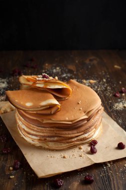 yığın krep katlanmış, gözleme, çilek, kurabiye, pudra şekeri ve koyu ahşap bir masa üzerine parşömen üzerine karamel şurup serpilir