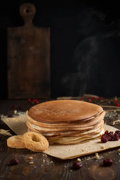 Una pila de panqueques, bayas, galletas y una tabla de cortar en pergamino sobre una mesa de madera oscura — Foto de Stock