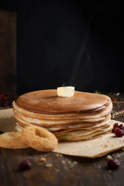 Una pila de panqueques, bayas, galletas, mantequilla y una tabla de cortar en pergamino sobre una mesa de madera oscura — Foto de Stock