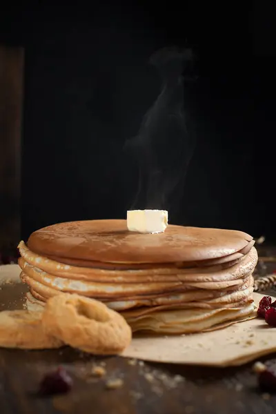 Una pila de panqueques, bayas, galletas, mantequilla y una tabla de cortar en pergamino sobre una mesa de madera oscura — Foto de Stock