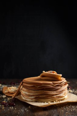 yığın krep katlanmış, gözleme, çilek, kurabiye, pudra şekeri ve koyu ahşap bir masa üzerine parşömen üzerine karamel şurup serpilir