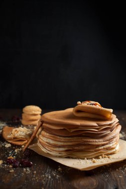 yığın krep katlanmış, gözleme, çilek, kurabiye, pudra şekeri ve koyu ahşap bir masa üzerine parşömen üzerine karamel şurup serpilir