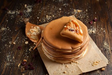 yığın krep katlanmış, gözleme, çilek, kurabiye, pudra şekeri ve koyu ahşap bir masa üzerine parşömen üzerine karamel şurup serpilir