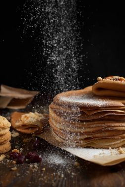 yığın krep katlanmış, gözleme, çilek, kurabiye, pudra şekeri ve koyu ahşap bir masa üzerine parşömen üzerine karamel şurup serpilir