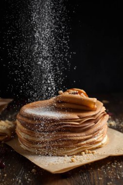 yığın krep katlanmış, gözleme, çilek, kurabiye, pudra şekeri ve koyu ahşap bir masa üzerine parşömen üzerine karamel şurup serpilir