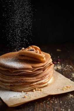 yığın krep katlanmış, gözleme, çilek, kurabiye, pudra şekeri ve koyu ahşap bir masa üzerine parşömen üzerine karamel şurup serpilir