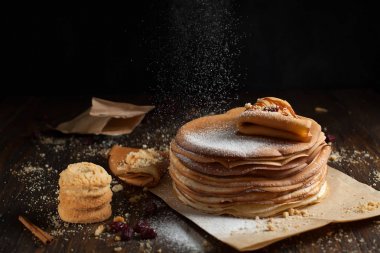 yığın krep katlanmış, gözleme, çilek, kurabiye, pudra şekeri ve koyu ahşap bir masa üzerine parşömen üzerine karamel şurup serpilir