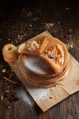 bir yığın krep, krep, çilek, kurabiye, pudra şekeri ve koyu ahşap bir masa üzerine parşömen üzerine karamel şurup serpilir iki katlanmış