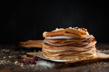 iki deste krep, krep, çilek, kurabiye, pudra şekeri ve koyu ahşap bir masa üzerine parşömen üzerine karamel şurup serpilir iki katlanmış