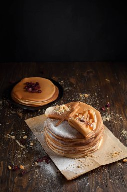 iki deste krep, krep, çilek, kurabiye, pudra şekeri ve koyu ahşap bir masa üzerine parşömen üzerine karamel şurup serpilir iki katlanmış