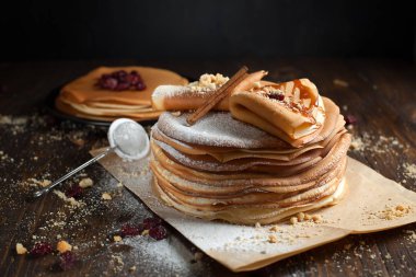 iki deste krep, krep, çilek, kurabiye, pudra şekeri ve koyu ahşap bir masa üzerine parşömen üzerine karamel şurup serpilir iki katlanmış