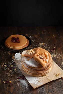 iki deste krep, krep, çilek, kurabiye, pudra şekeri ve koyu ahşap bir masa üzerine parşömen üzerine karamel şurup serpilir iki katlanmış