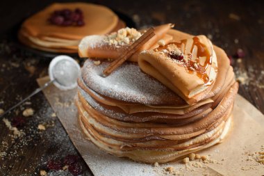 iki deste krep, krep, çilek, kurabiye, pudra şekeri ve koyu ahşap bir masa üzerine parşömen üzerine karamel şurup serpilir iki katlanmış