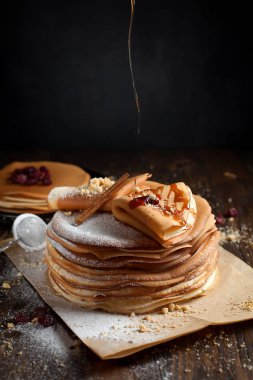 iki deste krep, krep, çilek, kurabiye, pudra şekeri ve koyu ahşap bir masa üzerine parşömen üzerine karamel şurup serpilir iki katlanmış