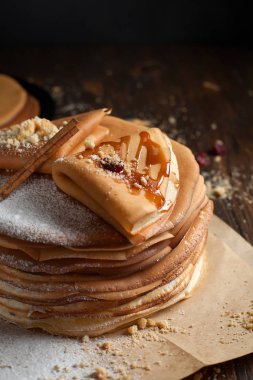iki deste krep, krep, çilek, kurabiye, pudra şekeri ve koyu ahşap bir masa üzerine parşömen üzerine karamel şurup serpilir iki katlanmış