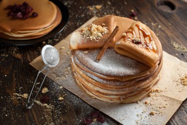 iki deste krep, krep, çilek, kurabiye, pudra şekeri ve koyu ahşap bir masa üzerine parşömen üzerine karamel şurup serpilir iki katlanmış