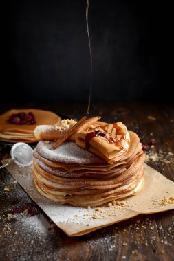 iki deste krep, krep, çilek, kurabiye, pudra şekeri ve koyu ahşap bir masa üzerine parşömen üzerine karamel şurup serpilir iki katlanmış