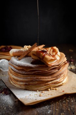 iki deste krep, krep, çilek, kurabiye, pudra şekeri ve koyu ahşap bir masa üzerine parşömen üzerine karamel şurup serpilir iki katlanmış