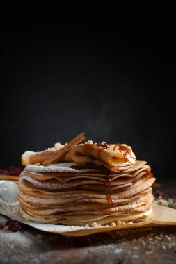 iki deste krep, krep, çilek, kurabiye, pudra şekeri ve koyu ahşap bir masa üzerine parşömen üzerine karamel şurup serpilir iki katlanmış