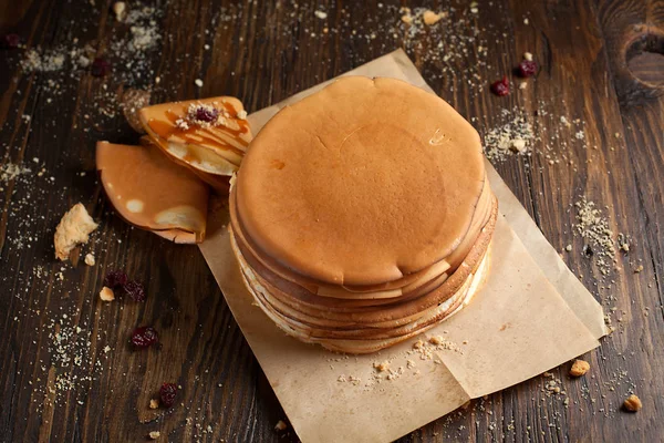 yığın krep katlanmış, gözleme, çilek, kurabiye, pudra şekeri ve koyu ahşap bir masa üzerine parşömen üzerine karamel şurup serpilir