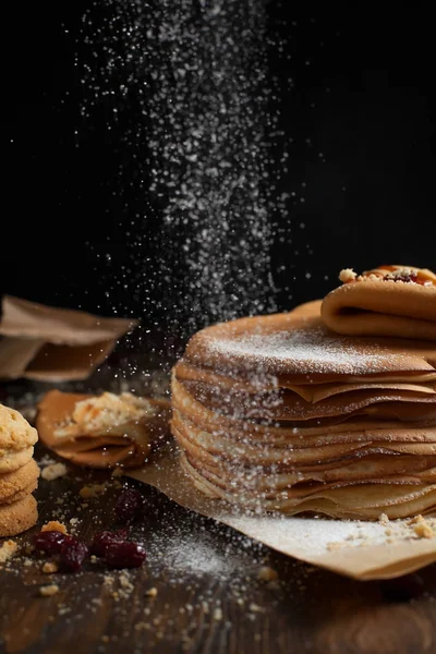 yığın krep katlanmış, gözleme, çilek, kurabiye, pudra şekeri ve koyu ahşap bir masa üzerine parşömen üzerine karamel şurup serpilir