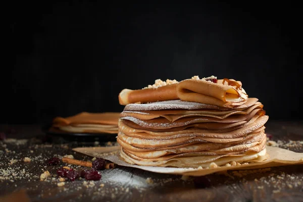 iki deste krep, krep, çilek, kurabiye, pudra şekeri ve koyu ahşap bir masa üzerine parşömen üzerine karamel şurup serpilir iki katlanmış