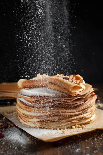 iki deste krep, krep, çilek, kurabiye, pudra şekeri ve koyu ahşap bir masa üzerine parşömen üzerine karamel şurup serpilir iki katlanmış