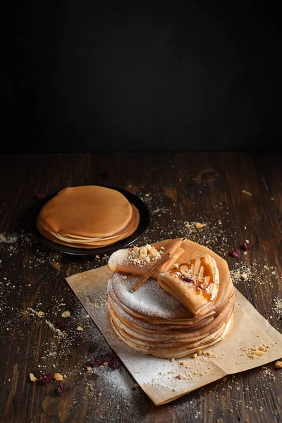 iki deste krep, krep, çilek, kurabiye, pudra şekeri ve koyu ahşap bir masa üzerine parşömen üzerine karamel şurup serpilir iki katlanmış