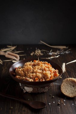 ekmek ve bir tahta kaşık ile ahşap bir masa üzerinde kahverengi bir seramik tabak pilav