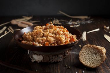 ekmek ve bir tahta kaşık ile ahşap bir masa üzerinde kahverengi bir seramik tabak pilav