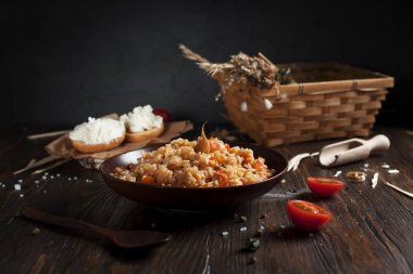 kahverengi bir seramik tabak, kiraz domates ve spikelets buğday, sepet pilav sandviç peynir ve koyu ahşap bir masa üzerinde bir tahta kaşık ile