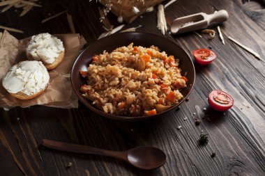kahverengi bir seramik tabak, cherry domates, beyaz peynir ile kızarmış ekmek ve koyu ahşap bir masa üzerinde bir tahta kaşık pilav