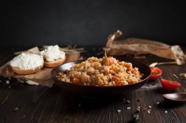 kahverengi bir seramik tabak, cherry domates, beyaz peynir ile kızarmış ekmek ve koyu ahşap bir masa üzerinde bir tahta kaşık pilav