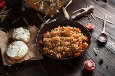 kahverengi bir seramik tabak, cherry domates, beyaz peynir ile kızarmış ekmek ve koyu ahşap bir masa üzerinde bir tahta kaşık pilav