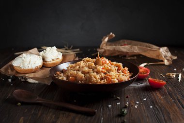 kahverengi bir seramik tabak, cherry domates, beyaz peynir ile kızarmış ekmek ve koyu ahşap bir masa üzerinde bir tahta kaşık pilav