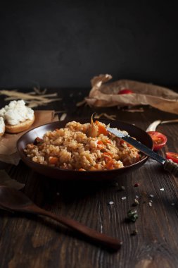 kahverengi bir seramik tabak, cherry domates, beyaz peynir ile kızarmış ekmek ve koyu ahşap bir masa üzerinde bir tahta kaşık pilav