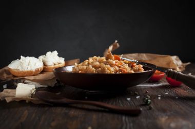 kahverengi bir seramik tabak, cherry domates, beyaz peynir ile kızarmış ekmek ve koyu ahşap bir masa üzerinde bir tahta kaşık pilav