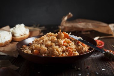 kahverengi bir seramik tabak, cherry domates, beyaz peynir ile kızarmış ekmek ve koyu ahşap bir masa üzerinde bir tahta kaşık pilav