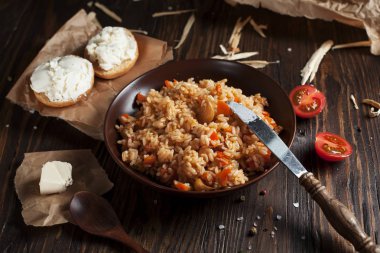 kahverengi bir seramik tabak, cherry domates, beyaz peynir ile kızarmış ekmek ve koyu ahşap bir masa üzerinde bir tahta kaşık pilav
