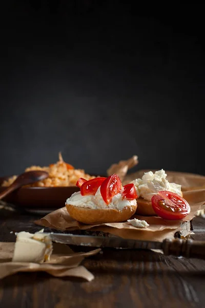 Тосты с сыром фета на выпечке бумаги, помидоры черри на фоне плова с овощами и курицей, на темном деревянном столе — стоковое фото