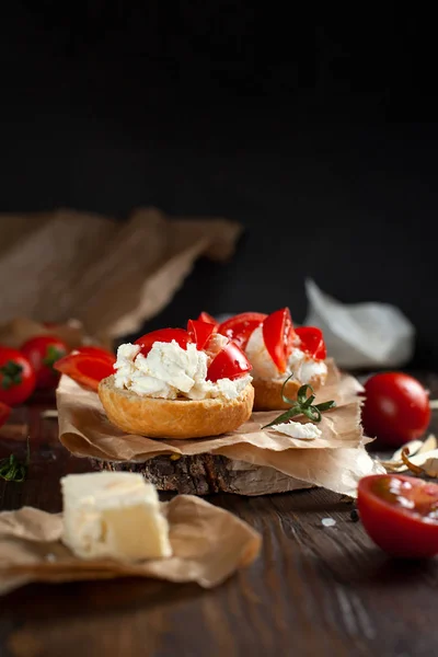 Тост с сыром фета на выпечке бумаги, помидоры черри и масло на темном деревянном столе — стоковое фото