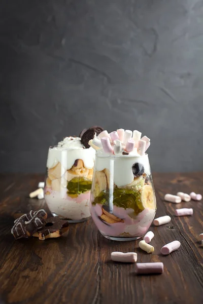 Sobremesa em um copo com uma banana, biscoitos, marshmallows e geleia em uma mesa de madeira — Fotografia de Stock