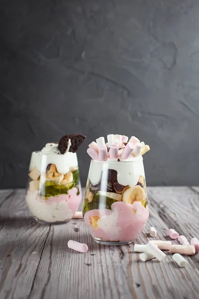 Sobremesa em um copo com uma banana, biscoitos, marshmallows e geleia em uma mesa de madeira — Fotografia de Stock