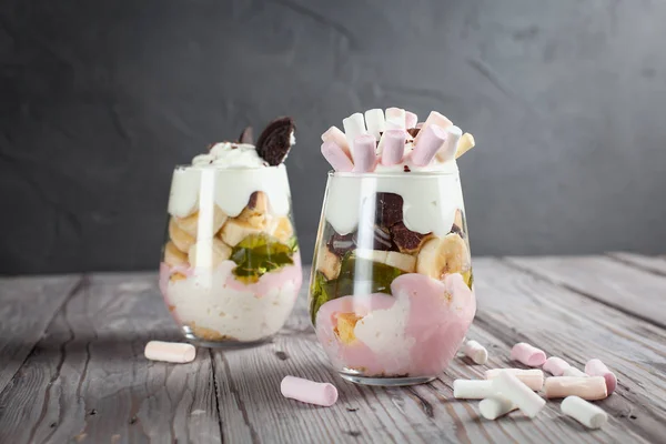 Sobremesa em um copo com uma banana, biscoitos, marshmallows e geleia em uma mesa de madeira — Fotografia de Stock