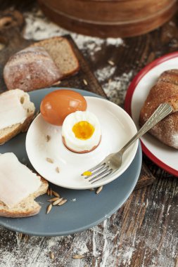 ahşap bir masa üzerinde pastırmalı bir tabak, taze pişmiş ekmek ve sandviç haşlanmış yumurta
