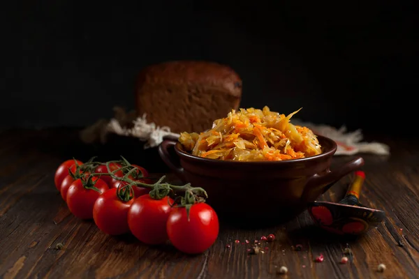 Тушеная капуста, хлеб и помидоры черри на темном деревянном столе — стоковое фото