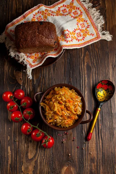 Тушеная капуста, хлеб и помидоры черри на темном деревянном столе — стоковое фото